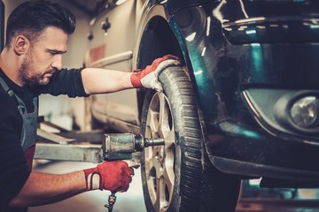 Professional car mechanic changing car wheel in auto repair service.