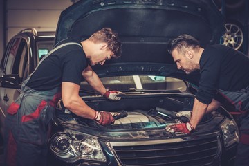 Professional car mechanics checking under hood in auto repair service.