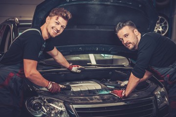 Professional car mechanics checking under hood in auto repair service.