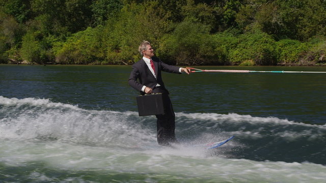 Businessman with briefcase water skiing to work, slow motion