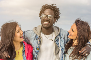 Group of multiracial friends smiling outdoor - a black guy is hugging two caucasian girls - multiracial, friends and lifestyle concept