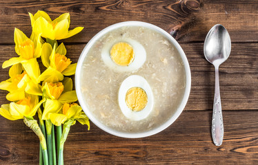 Traditional easter soup white borscht with eggs on wooden table