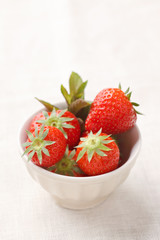 Fresh strawberries in a porcelain bowl on linen tablecloth