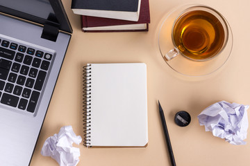 Office table desk with supplies, white blank note pad, cup, pen, pc, crumpled paper, flower on wooden background. Top view