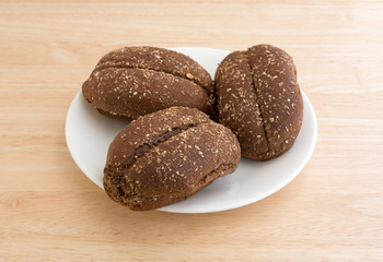 Multi-grain rolls on a white plate atop a wood table top side view.