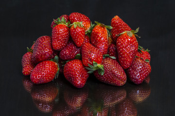 Heap of  fresh strawberries placed on a mirror black wooden table reflected on it