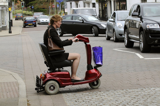 Woman Seated On A Mobility Scooter Crosses The Road At A Pedestrian Crossing