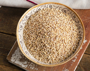 Barley in ceramic bowl on a wooden board.