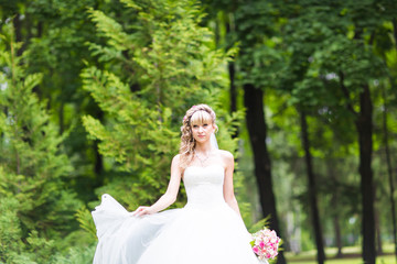Fototapeta na wymiar Beautiful bride with wedding bouquet of flowers outdoors in green park.