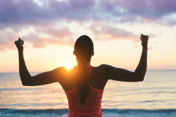 Fitness woman celebrating fitness workout success and motivation towards the sea and sunset.