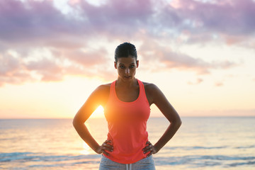 Fitness woman motivation. Challenging and motivating looking female athlete  with the sun and sea behind.