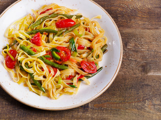 Tagliatelle pasta with vegetables on a wooden background.