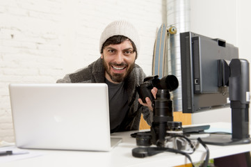 young attractive press photographer holding photographic camera viewing his work on editor office desk