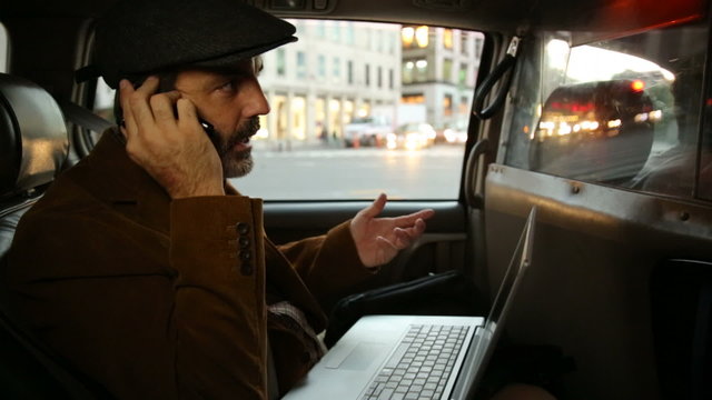 Businessman in taxi uses laptop and cell phone
