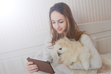 Girl with her dog on the bed with tablet.