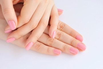 Closeup of hands of a young woman with pink manicure on nails against white background