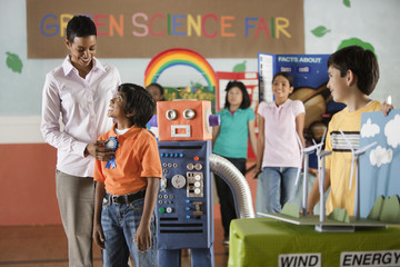 A group of students and a teacher awarding a prize to a boy standing beside a robot model, 