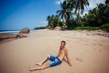 Man relaxing on a tropical beach. Young tanned man taking sunbat