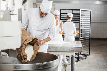 Mature Male Baker Pouring Flour In Kneading Machine