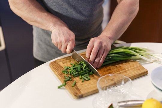 man chopped green onion on the board. Wooden table