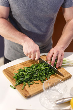 man chopped green onion on the board. Wooden table