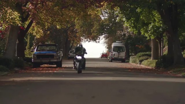 Man Riding Fast Motorcycle in City Streets Toward Camera in Fall Season