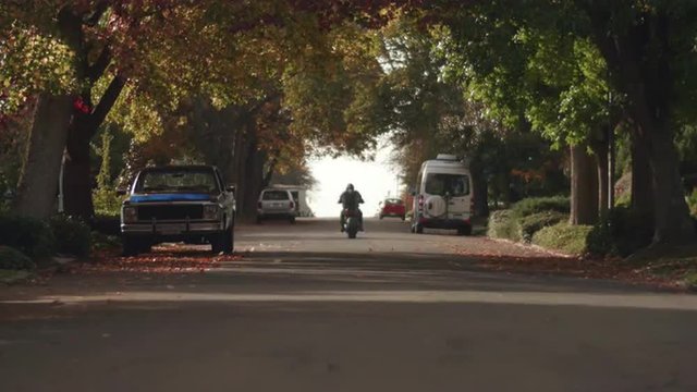 Man Riding Motorcycle Away from Camera and Standing Up in Fall Season