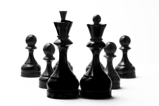 Chess black king and queen before few black pawns on a white background