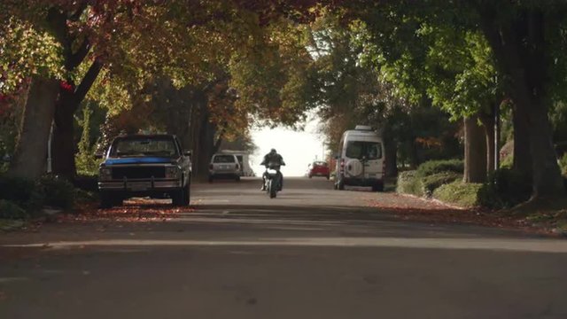 Man Riding Motorcycle in City Streets Toward Camera in Fall Season
