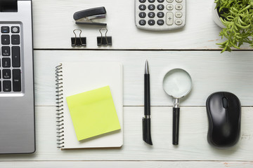 Office desk table with supplies. Top view. Copy space for text. Laptop, notepad, pen, magnifying glass, calculator, remindmer, flower.
