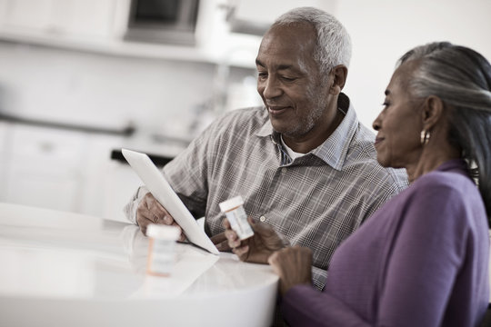 A grey haired couple sitting at a table, looking at information on a digital tablet, 