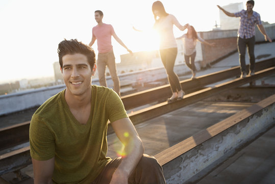 A group of people on a rooftop in the city at dusk, balancing and walking along steel struts on the roof,
