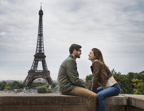 Couple sitting facing each other on wall in with Eiffel Tower in  background, Paris, France