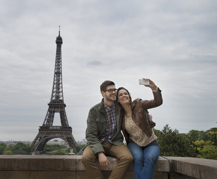 Couple sitting side by side taking selfie with Eiffel Tower in  background