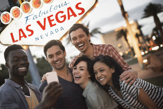 A group of five friends, men and women posing under the Las Vegas sign,