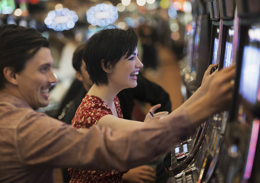 Two people, a young man and woman, playing the slot machines in a casino, 