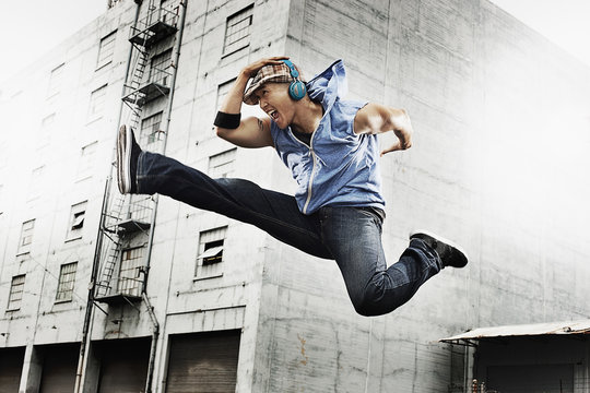 A young man doing a karate kick, one leg outstretched and one leg bent up, wearing earphones,