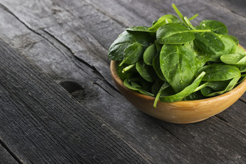 Spinach leaves in bowl on dark wooden background