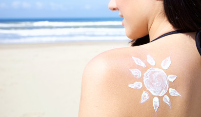 Cute young woman smiling on the beach in bikini with sun painted with cream on the back closeup