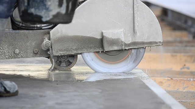 Worker using a circular disk cutter to cut joints in the concrete floor on a construction site in a noisy wet and dusty environment 