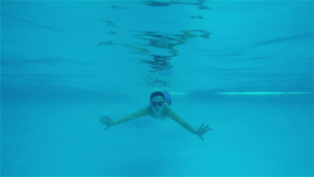Teen boy swimming underwater in pool.