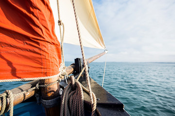 rope wound on a wooden cleat fixed on the hull of a rigging vintage sailing boat with a beige jib...