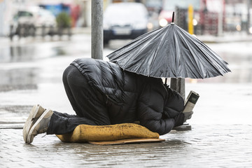 Homeless beggar with umbrella in the rain