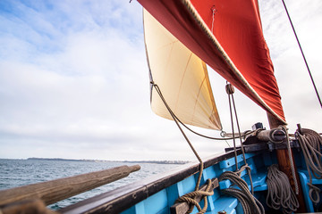 beige cotton jib sail and an ocher sail filled by the wind with wooden mast, bowsprit and hull of an old rigging sailing boat during a sunny sea trip in brittany