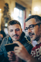 Two men siting in the cafeteria and looking into smart phone.
