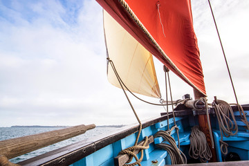 beige cotton jib sail and an ocher sail filled by the wind with wooden mast, bowsprit and hull of...