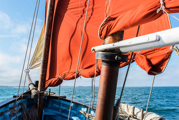 bow of an old wooden blue sailing boat with a cotton vintage ocher sails, wooden mast, white jib...