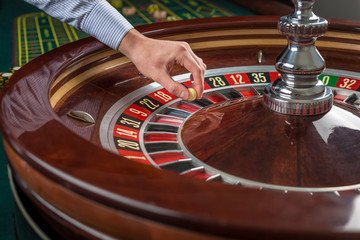 Roulette wheel and croupier hand with white ball in casino 