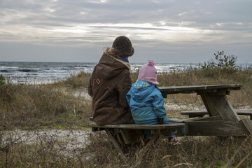 Kvinna och barn vilar ut p&aring; b&auml;nk p&aring; sandstrand