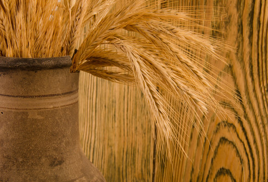 Old crock with a bunch of wheat ears (against the background of a wooden wall, with focus on wheat ears), retro style